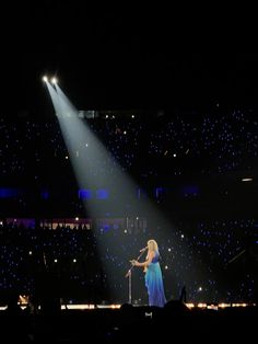 a woman standing on top of a stage in front of a microphone and spotlights