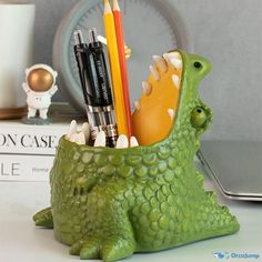 a green dragon shaped pen holder with pencils and markers in it's mouth