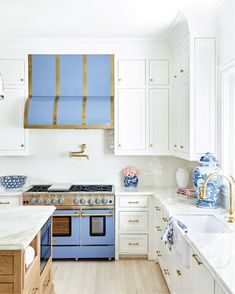 a white kitchen with blue and gold accessories on the stove top, oven hood, and cabinets