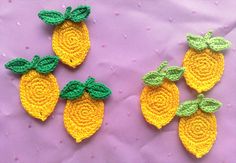 three crocheted lemons on a purple surface with green leaves and yellow ones