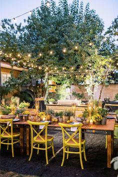 an outdoor dining area with yellow chairs and lights strung from the trees over the table