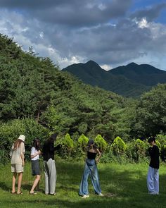 four people are standing in the grass looking at trees and mountains on a cloudy day