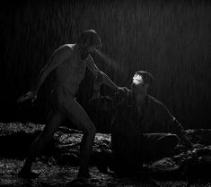 two men in the rain, one is holding an umbrella and the other is kneeling down