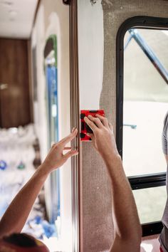 two people are painting the side of a bus with white paint and red tape on it