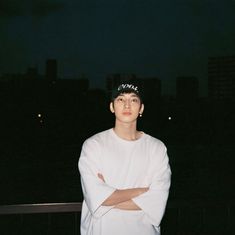 a young man standing with his arms crossed in front of the camera at night time