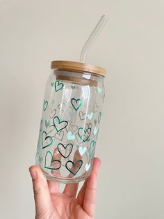 a hand holding a mason jar with hearts painted on the side and a straw in it