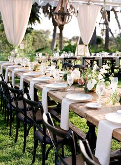 a long table set up with place settings and flowers on it for an outdoor wedding reception