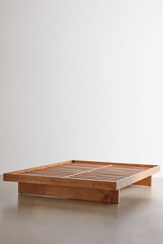 a wooden bed frame sitting on top of a cement floor next to a white wall