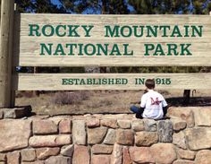 a man sitting on top of a rock wall next to a sign that says rocky mountain national park