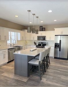 a large kitchen with white cabinets and stainless steel appliances, along with an island in the middle