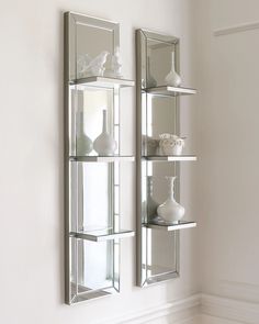 two mirrors mounted to the side of a wall next to vases and other items