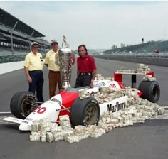 two men standing next to a race car with stacks of money on the front wheel