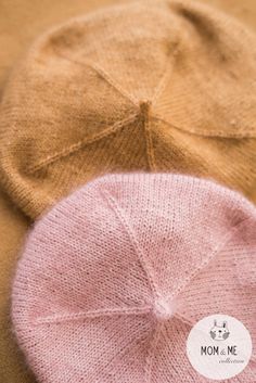 two knitted hats sitting next to each other on top of a brown tablecloth