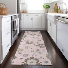 a kitchen area with white cabinets and wooden floors, along with a pink rug on the floor