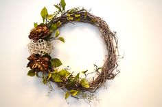 a wreath with pine cones and greenery is displayed on a white wall behind it