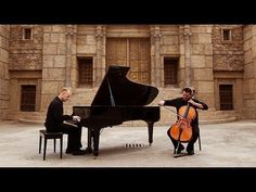 two men playing instruments in front of a grand piano