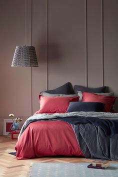 a bed with red and grey sheets in a bedroom next to a lamp on the wall