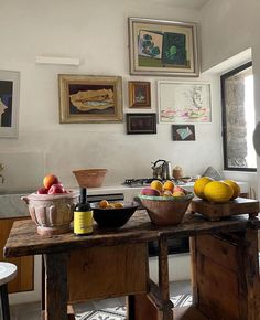 a table with bowls of fruit on it in a room filled with pictures and paintings