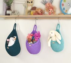 three crocheted purses hanging on a wall with stuffed animals and toys in them