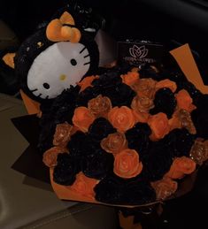 a hello kitty stuffed animal sitting next to a bouquet of orange and black rosettes