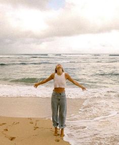 a woman standing on top of a sandy beach next to the ocean with her arms outstretched