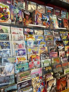 there are many comic books on display in the store front window and behind it is a wall full of comics