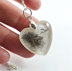 a hand holding a heart shaped pendant with a fingerprint on it