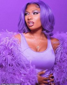 a woman with purple feathers on her body posing for a photo in front of a purple background