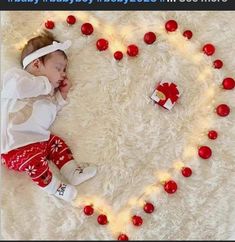 a baby laying on top of a white rug next to a heart made out of ornaments