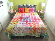 a bed with a colorful quilt on top of it next to two nightstands and lamps