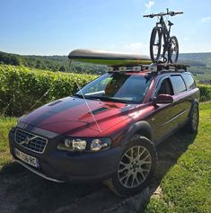 a car with a bike on top of it parked in front of a vineyard field