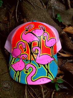 a pink and blue hat with flamingos on it sitting on the ground next to leaves