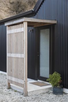 a black building with a white door and a potted plant on the ground next to it