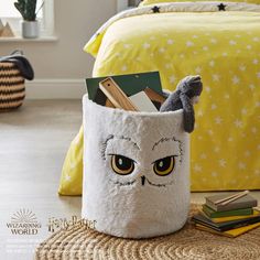 an owl themed storage bin sits on the floor in front of a bed with yellow sheets and pillows