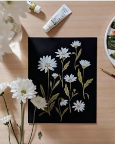 some white flowers are sitting on a table next to paintbrushes and water bottles