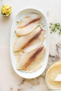 fish fillets on a plate next to a bowl of dressing