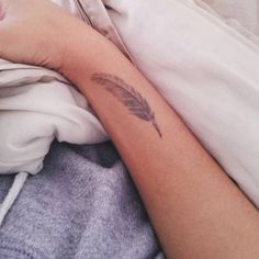 a woman laying in bed with her arm wrapped around a feather tattoo on her left arm