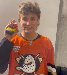 a man in an orange hockey jersey holding a yellow and black object