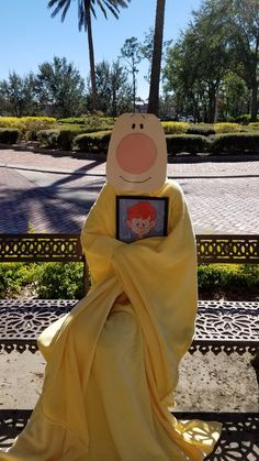 a person in a yellow dress sitting on a bench with a stuffed animal covering their face