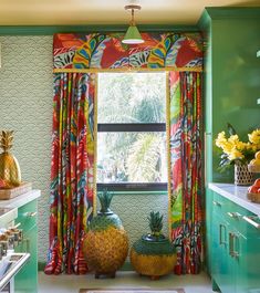 two pineapples sit in front of a window with colorful drapes and curtains