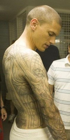 a man with tattoos on his back looking down at his cell phone while standing in front of other men