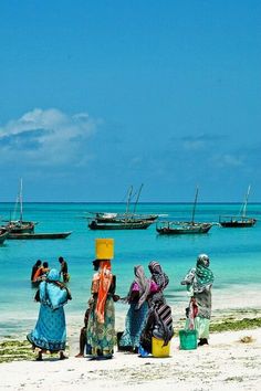 several people standing on the beach with boats in the water behind them and one person carrying a bucket