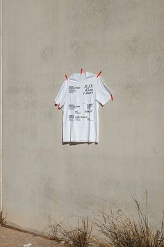 a white t - shirt hanging on the side of a building with red pins attached to it