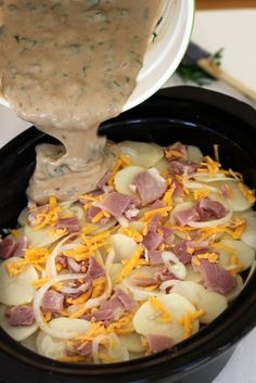 a crock pot filled with potatoes, ham and gravy being poured into it