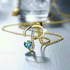 a gold necklace with a blue heart on it and a diamond in the shape of a letter