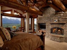 a bedroom with a stone fireplace in the center and wood beams on the ceiling, along with large windows