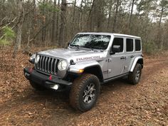 a silver jeep driving down a dirt road in the woods