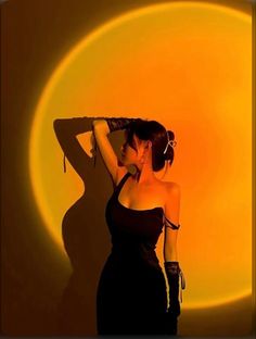 a woman in a black dress is posing with her arms behind her head and the sun shining down on her