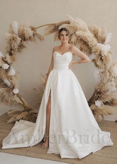 a woman in a white wedding dress standing next to a large wreath with feathers on it