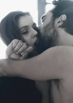 a man and woman kissing each other while they are in black and white photo with sunlight streaming through the window behind them